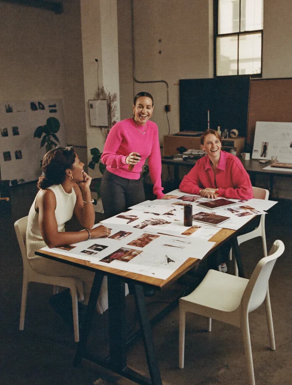 Three creatives laughing around a studio table covered in printed photo frames and sketches